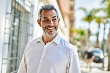 Middle age grey-haired man smiling happy standing at the city.