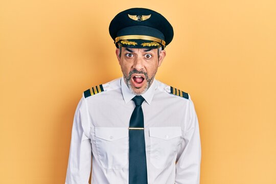 Handsome middle age man with grey hair wearing airplane pilot uniform afraid and shocked with surprise and amazed expression, fear and excited face.
