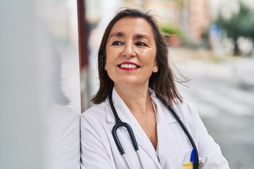 Middle age woman wearing doctor uniform smiling confident standing at street
