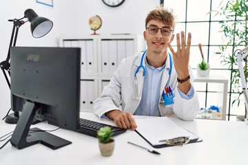 Obraz premium Young caucasian doctor man working at the clinic showing and pointing up with fingers number four while smiling confident and happy.