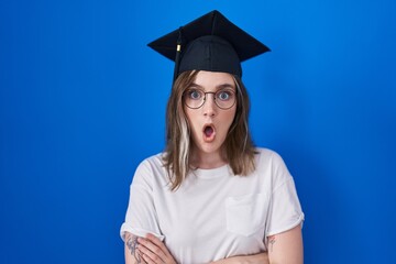 Blonde caucasian woman wearing graduation cap afraid and shocked with surprise expression, fear and excited face.