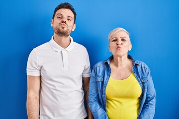 Fototapeta premium Young brazilian mother and son standing over blue background looking at the camera blowing a kiss on air being lovely and sexy. love expression.