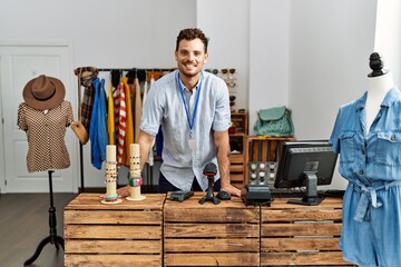 Young hispanic shopkeeper man smiling happy standing by counter at clothing store.