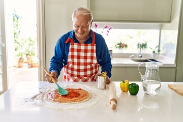 Senior man smiling confident cooking pizza at kitchen