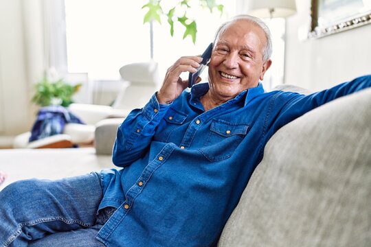 Senior man with grey hair sitting on the sofa at the living room of his house having a conversation speaking on the phone