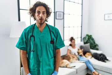 Young veterinarian man checking dogs at home scared and amazed with open mouth for surprise,...