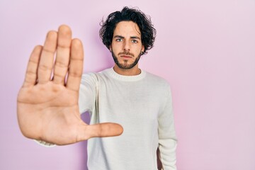 Fototapeta premium Handsome hispanic man wearing casual white sweater doing stop sing with palm of the hand. warning expression with negative and serious gesture on the face.