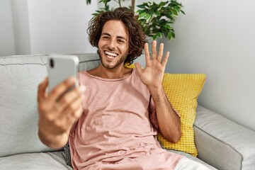 Young hispanic man smiling happy having video call using smartphone sitting on the sofa at home.