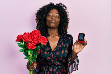 Young african american woman holding bouquet of flowers and engagement ring looking at the camera...