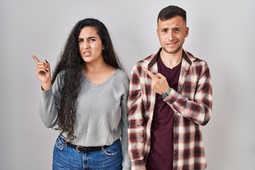 Young hispanic couple standing over white background pointing aside worried and nervous with forefinger, concerned and surprised expression