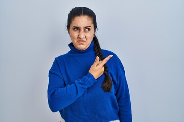 Young hispanic woman standing over isolated background pointing aside worried and nervous with...