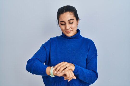 Young hispanic woman standing over isolated background checking the time on wrist watch, relaxed and confident