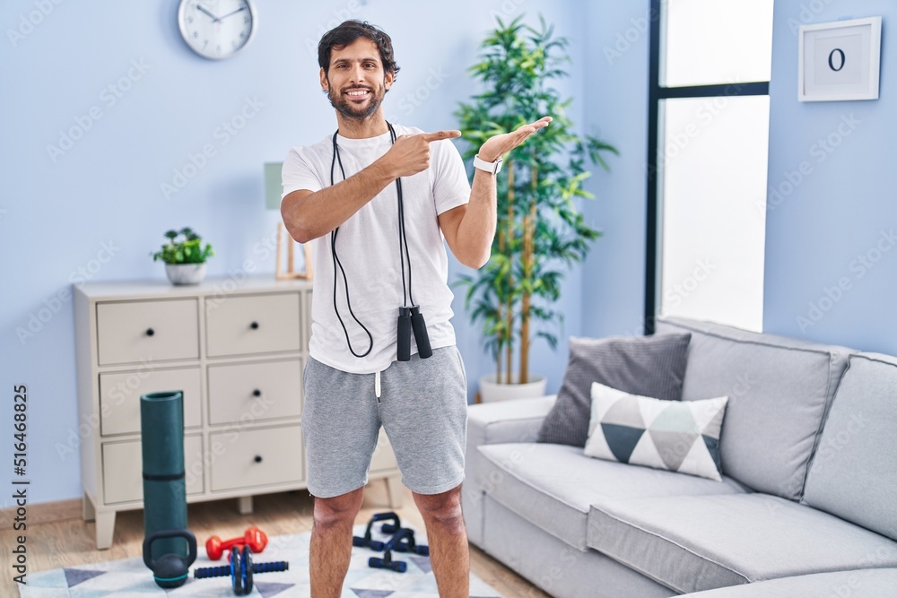 Sticker Handsome latin man wearing sportswear at home amazed and smiling to the camera while presenting with hand and pointing with finger.