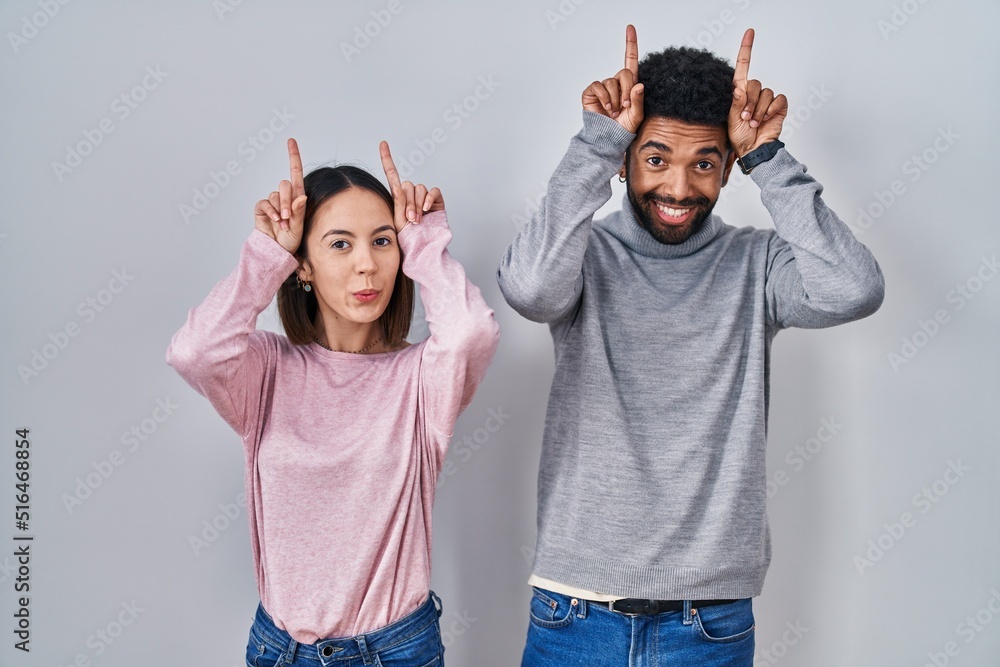 Sticker Young hispanic couple standing together doing funny gesture with finger over head as bull horns