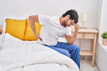 Young hispanic man suffering for back ache sitting on bed at bedroom