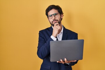 Handsome latin man working using computer laptop looking confident at the camera smiling with crossed arms and hand raised on chin. thinking positive.