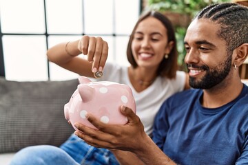 Man and woman couple smiling confident insert coin on piggy bank at home