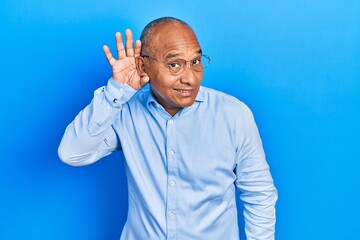 Middle age latin man wearing casual clothes and glasses smiling with hand over ear listening an hearing to rumor or gossip. deafness concept.