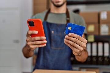 Young hispanic man business worker using smartphone and credit card at storehouse