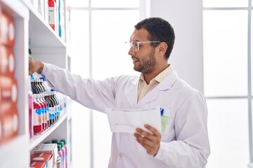 Naklejka na ściany i meble Young man pharmacist organize shelving reading shelving at pharmacy