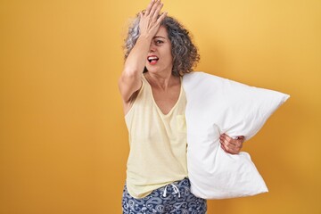 Middle age woman with grey hair wearing pijama hugging pillow surprised with hand on head for...