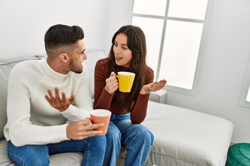 Young hispanic couple drinking coffee sitting on the sofa at home.