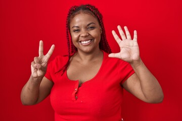 African american woman with braided hair standing over red background showing and pointing up with fingers number seven while smiling confident and happy.