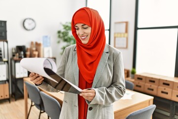 Young woman wearing arabic scarf reading document at office