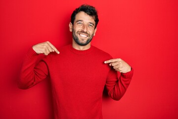 Handsome man with beard wearing casual red sweater looking confident with smile on face, pointing oneself with fingers proud and happy.
