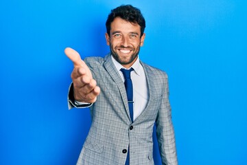 Handsome man with beard wearing business suit and tie smiling friendly offering handshake as greeting and welcoming. successful business.