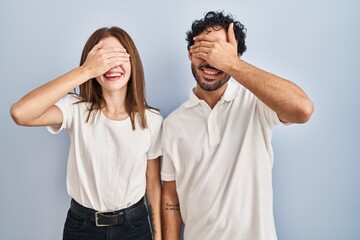 Young couple wearing casual clothes standing together smiling and laughing with hand on face covering eyes for surprise. blind concept.