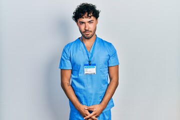 Young hispanic man wearing blue male nurse uniform skeptic and nervous, frowning upset because of...