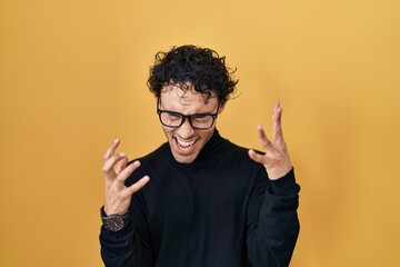 Hispanic man standing over yellow background celebrating mad and crazy for success with arms raised...