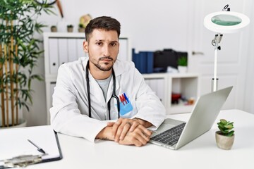 Young doctor working at the clinic using computer laptop skeptic and nervous, frowning upset because of problem. negative person.