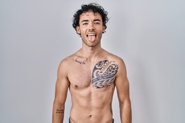 Hispanic man standing shirtless sticking tongue out happy with funny expression. emotion concept.