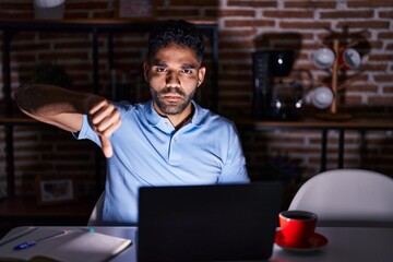 Hispanic man with beard using laptop at night looking unhappy and angry showing rejection and...