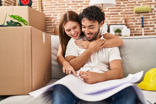Man and woman couple hugging each other looking house plans at new home