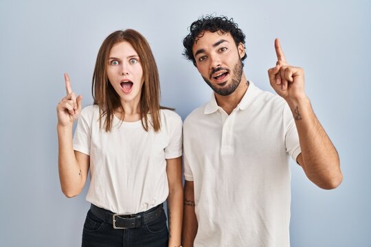 Young couple wearing casual clothes standing together pointing finger up with successful idea. exited and happy. number one.