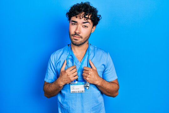 Young hispanic man wearing blue male nurse uniform skeptic and nervous, frowning upset because of problem. negative person.