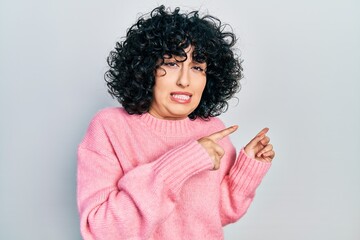 Young middle east woman wearing casual clothes pointing aside worried and nervous with both hands,...