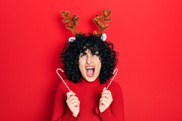 Young middle east woman wearing cute christmas reindeer horns angry and mad screaming frustrated...