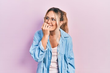 Beautiful young blonde woman wearing casual clothes and glasses looking stressed and nervous with hands on mouth biting nails. anxiety problem.