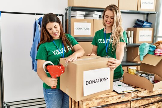 Two young volunteers woman smiling happy packing donations box at charity center.