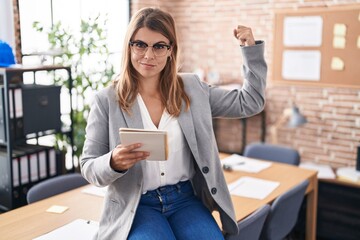 Young hispanic woman working at the office wearing glasses strong person showing arm muscle, confident and proud of power