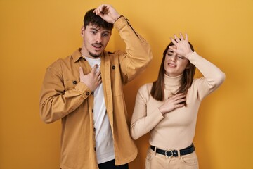 Young hispanic couple standing over yellow background touching forehead for illness and fever, flu and cold, virus sick