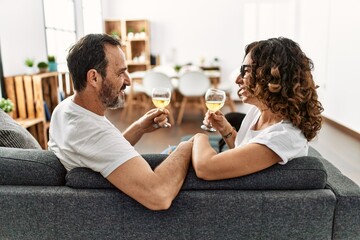 Middle age hispanic couple smiling happy toasting with champagne. Sitting on the sofa at home.