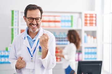 Middle age hispanic man working at pharmacy drugstore celebrating surprised and amazed for success...