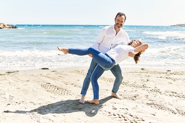 Middle age hispanic couple smiling happy dancing at the beach.