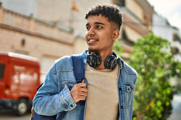 Hispanic young man smiling wearing headphones at the street