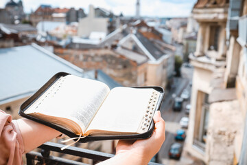 Open Bible in hands on the background of the city